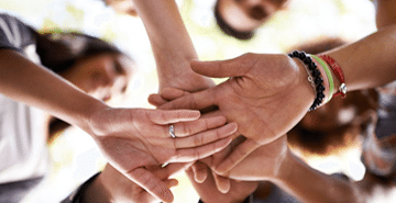 Five people put their hands on top of each other in a huddle.