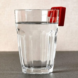 A red, EZ Fill Liquid Level Indicator rests on the edge of a drinking glass filled with water.