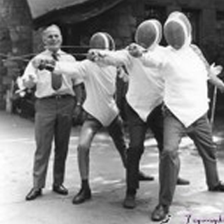 A black and white photo of the Carroll Center for the Blind’s first fencing team wearing full fencing gear, standing with their instructor, Larry Dargie.