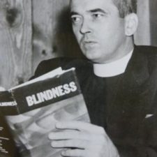 A black and white photo of Father Carroll holding up a copy of his newly published book.