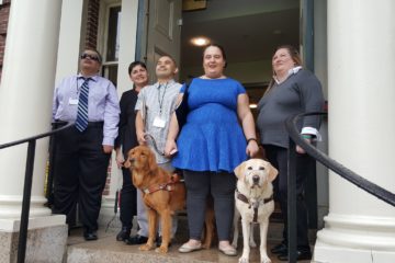 A group of five blind and visually impaired adults smile together at the top of stairs at Radcliffe Institute for Advanced Study.