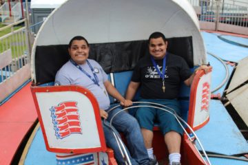 During an exclusive event at the Waltham Lions Club Carnival, two clients smile widely while riding on the tilt-a-whirl spinning teacup ride.