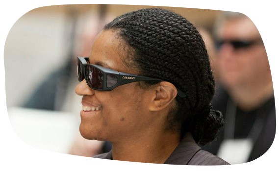 A blind woman wearing sunglasses laughs with others at an advocacy event at the Massachusetts State House.