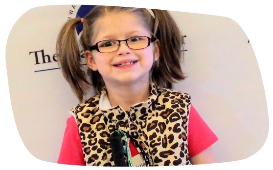 A young girl with visual impairment smiles while holding up her cane at the New England Regional Braille Challenge.