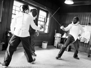 At the Carroll Center for the Blind, two fencers wearing full pads and gear touch epees as they begin a match.