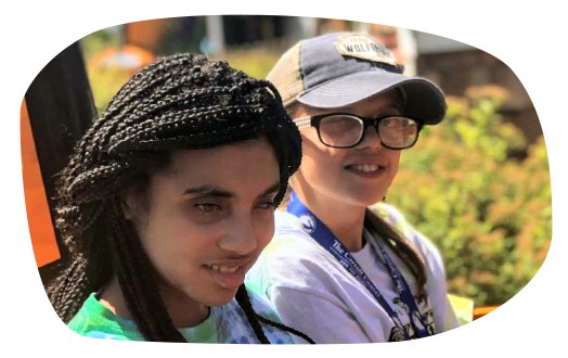 Two teenage girls with visual impairments smile together on a ride at an amusement park.