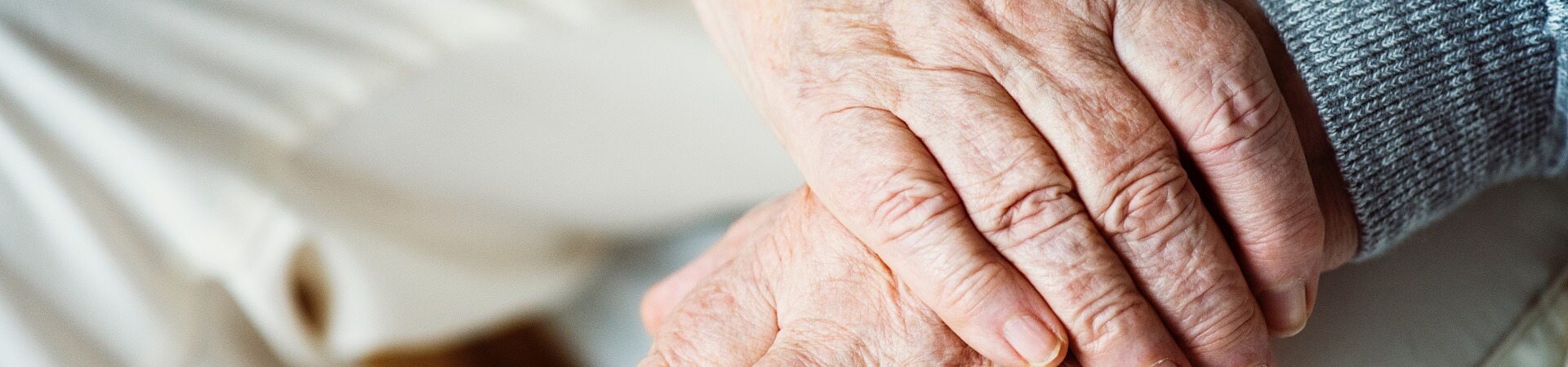 The hands of an elderly person interlock atop their lap.