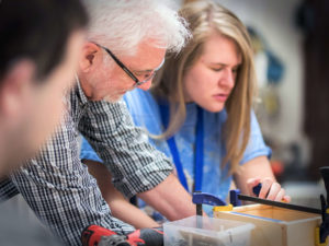 Bill Reynolds (left), Manual Arts Instructor at the Carroll Center for the Blind, teaches a young woman (right) who is blind about safe tool use in the wood shop.