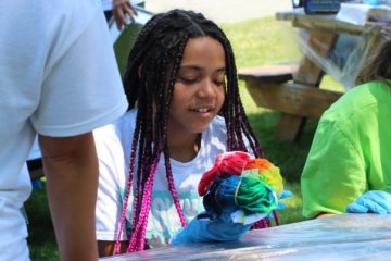 A female teenager in the Carroll Center's summer program smiles while tie-dying a shirt.