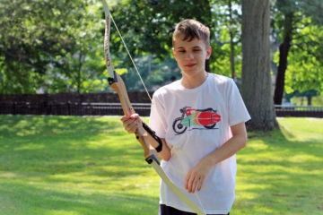 A male teen summer camper holds up a bow during archery at the Carroll Center's Field day.