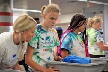 In the airport security line, two female campers in the Carroll Center's summer programs load their belongings into trays.