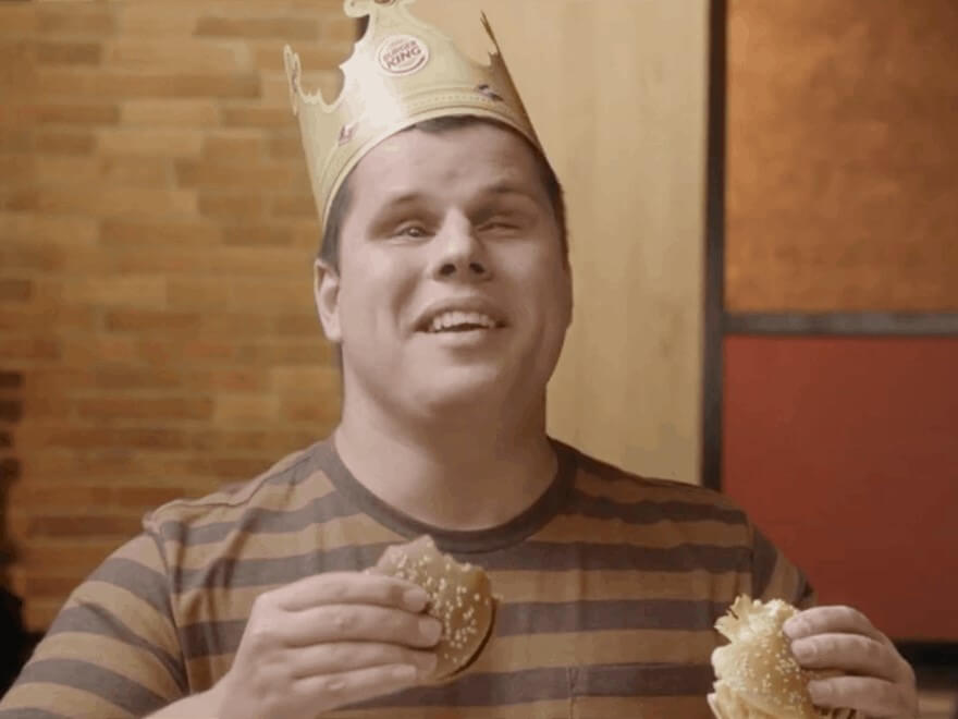 In the Brazil Burger King commercial, a blind man wearing a Burger King paper crown smiles while double-fisting two burgers.
