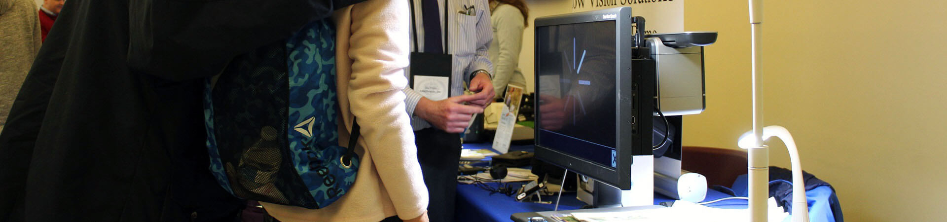 A vendor demonstrates an electronic desktop magnifier to two attendees at the Assistive Technology Fair.