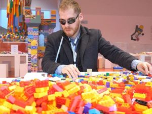 Matthew Shifrin, who has been working tirelessly for several years to spread audio and Braille Lego building instructions to children around the world, sits at a table filled with Lego blocks.