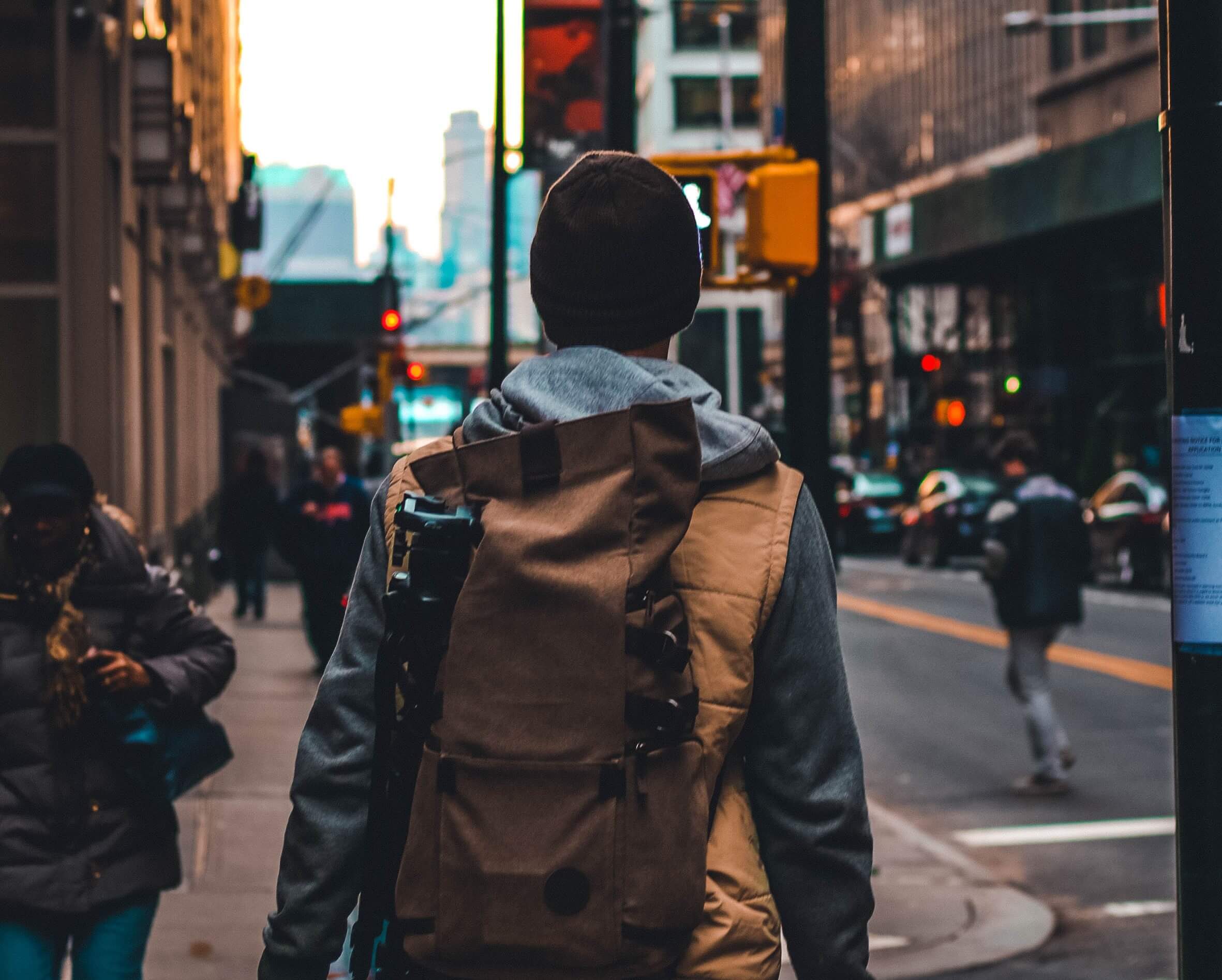 A man with his back facing the camera walks through a crosswalk in a bustling city.