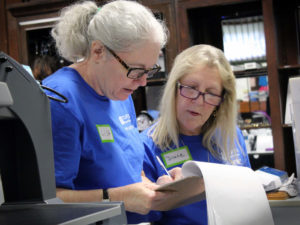 Two female volunteers glance down at a clipboard while helping with inventory in The Carroll Store.