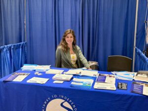 A staff member behind a Carroll Center for the Blind booth, filled with flyers.