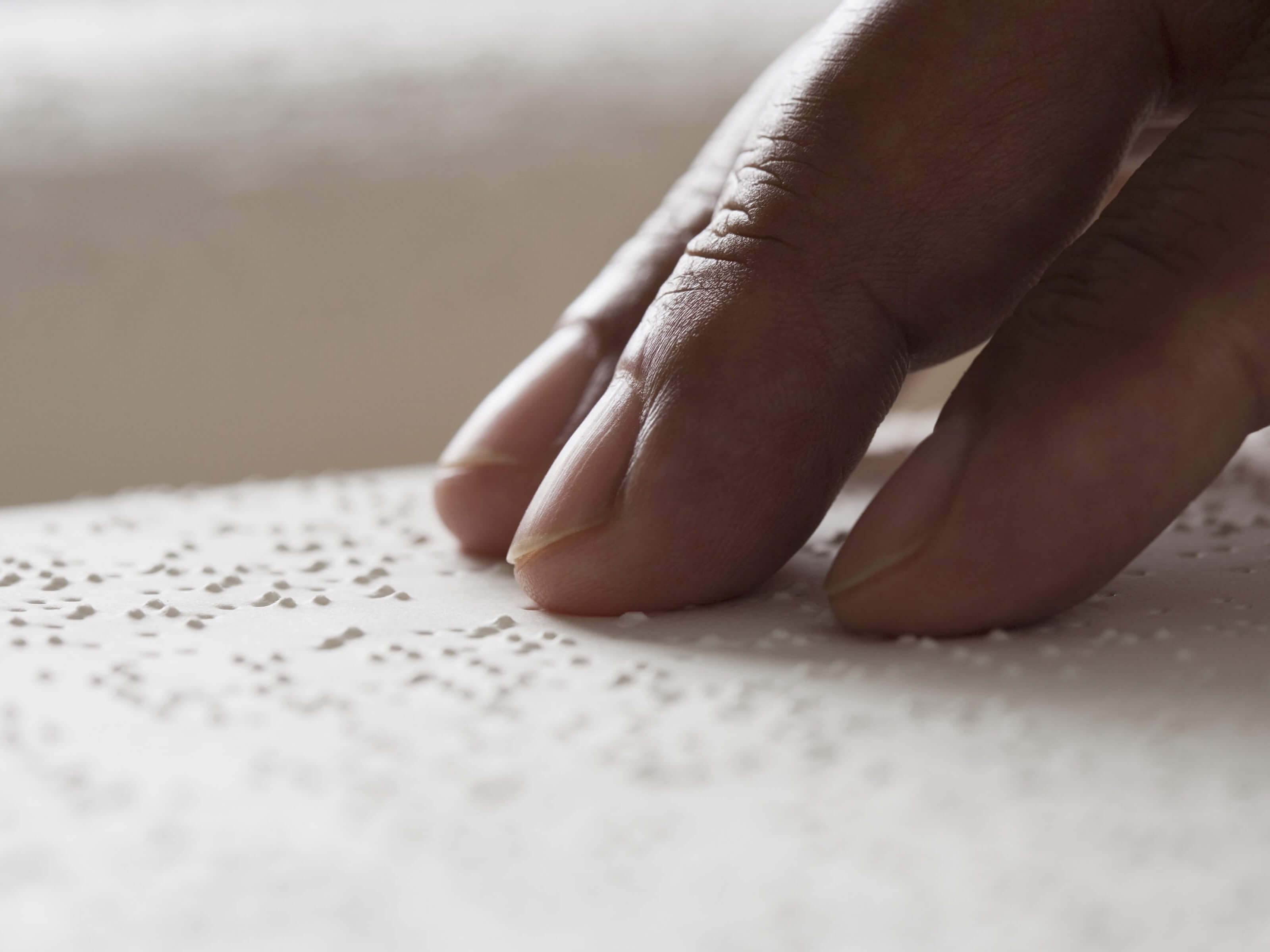 A hand rests on a sheet of braille.