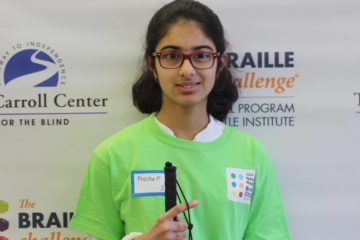 Sophomore group winner, Prasha Parajuli, poses in front of a braille challenge banner while wearing a green braille challenge shirt.