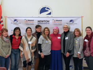 A group of 9 staff and volunteers pose in front of a banner at the Braille challenge.