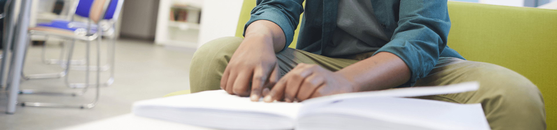 College student reading a braille textbook in a dorm lounge.