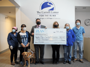 In the lobby of the Carroll Center for the Blind, Joan McGrath, executive director of PLAN of MA & RI presents Greg Donnelly, President & CEO of the Carroll Center for the Blind with a giant cardboard check.