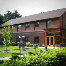 View of the newly constructed Technology Center. It's a large, modern wooden structure surrounded by green shrubbery.