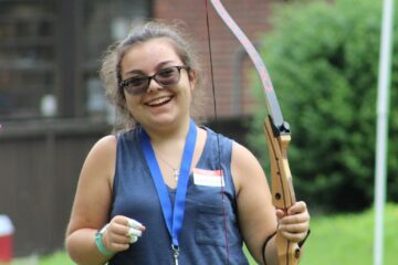 A teenager in the youth in transition program smiles widely after firing an arrow during archery.