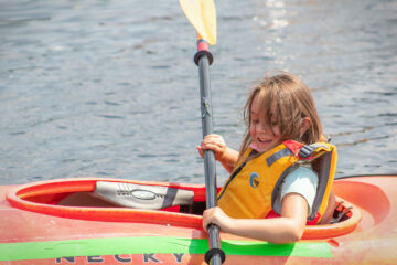As she floats in her kayak, a Carroll Kids student smiles widely as she paddles.
