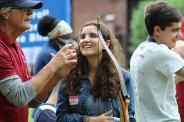 A teenager in the youth in transition program smiles contently as she turns towards her instructor after firing an arrow during archery.