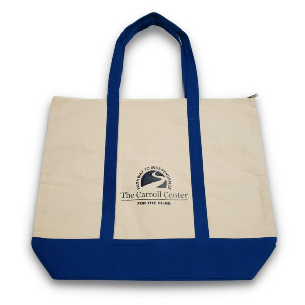Carroll Center for the Blind Tote Bag features beige canvas material on the body of the tote. The handles and bottom of the tote bag are blue. A small, black Carroll Center for the Blind logo appears on the middle of the tote.