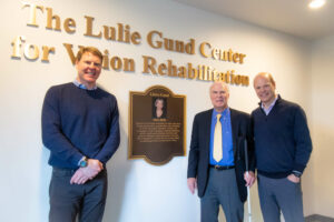From left to right, Zack, Gordon and Grant Gund pose together in front of a plaque of Lulie Gund in the newly dedicated Lulie Gund Center for Vision Rehabilitation foyer. 