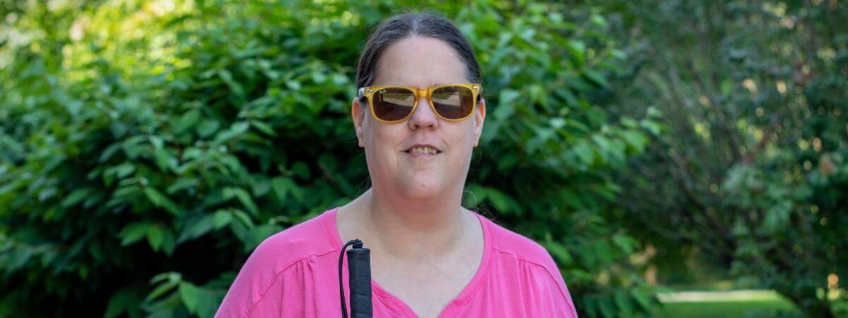 Hope Paulos smiles in front of green shrubbery at the Carroll Center for the Blind.