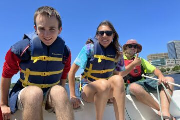 2 Carroll kids and a teacher all wearing life vests on a sail boat.