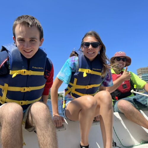 2 Carroll kids and a teacher all wearing life vests on a sail boat.