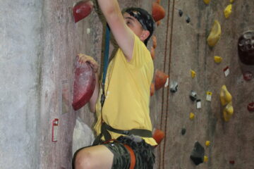 Yellow shirted boy practicing his technique on the lower parts of a rock climbing wall