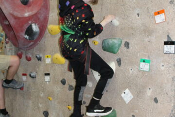 Polka dotted teenage scaling down a rock climbing wall