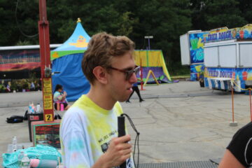Teen boy with tie dye shirt in front of a few carnival booths