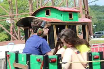 Boy in blue shirt with headphones next to girl in yellow shirt riding train roller coaster ride