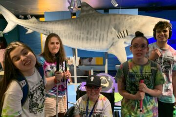 5 tie dye wearing teenagers in front of a full scale model of a whale shark