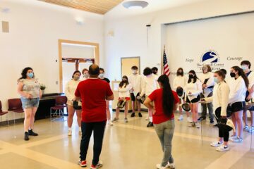 2 red shirted instructors teaching fencing in a white room to white garbed students