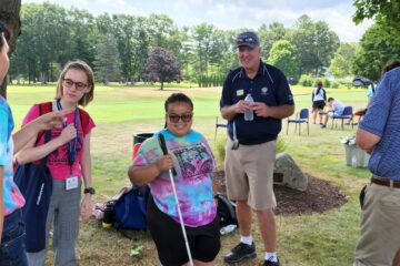Teen girl in tie dye shirt posing next to golf instructor