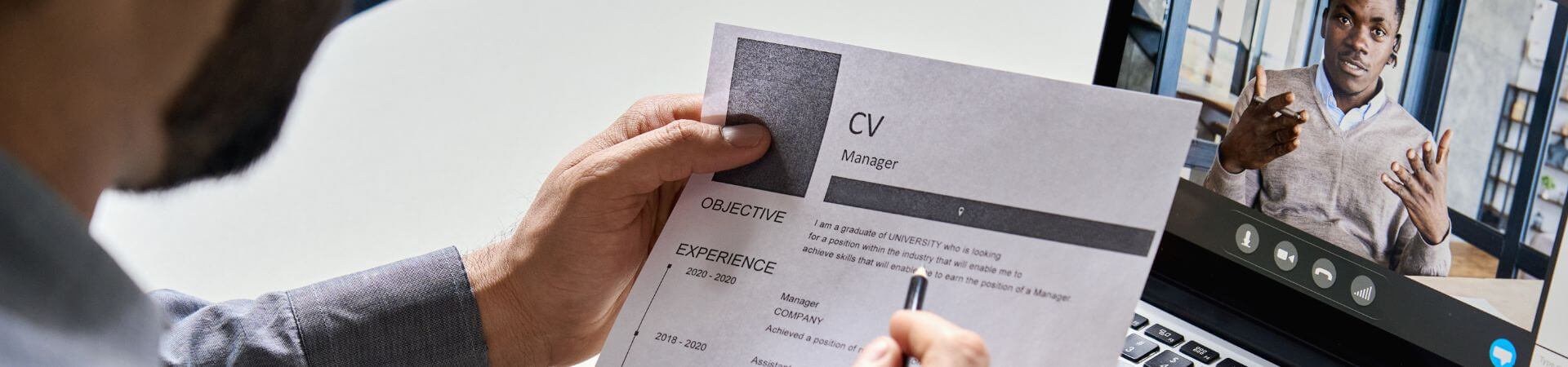A person holds up their resume while attending a virtual job fair on their laptop.