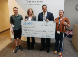 A client and staff member with blindness help the Carroll Center’s President & CEO and PLAN’s Executive Director hold a giant check from PLAN.