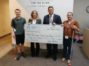 A client and staff member with blindness help the Carroll Center’s President & CEO and PLAN’s Executive Director hold a giant check from PLAN.