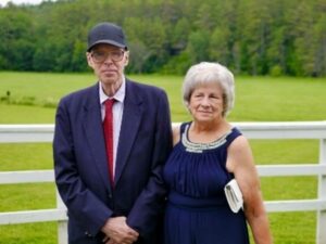 Peter and Deborah Coogan pose together in front of a white fence with a forest behind it.