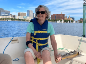 An older woman smiles as she steers a sailboat.