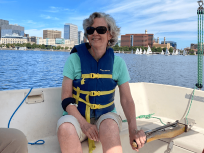 An older blind woman smiles as she steers a sailboat.