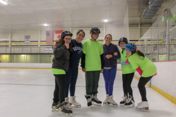 4 smiling teens and 2 instructors posing for a photo on the ice skating rink