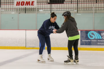 An instructor holding a girl's hands while they skate on the ice skating rink